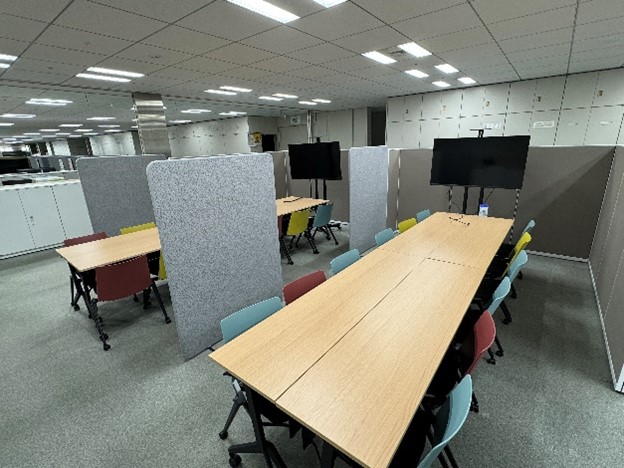 交通局建設工務部における、未来型オフィスの整備事例。ミーティング用のスペースとして長い机と椅子12脚が置かれており、これらが2つ、パーティションでそれぞれ分けられて配置されている。